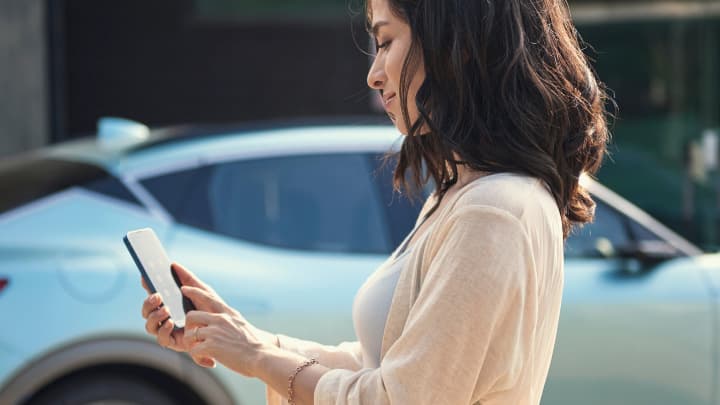 Woman looking at her phone with a car parked in the background