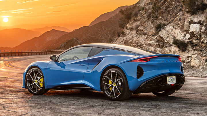 Rear stationary shot of a blue Lotus Emira with a sunset background