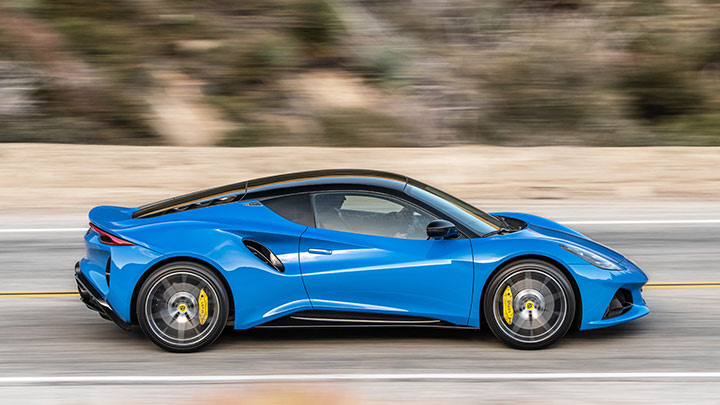 Side driving shot of a blue Lotus Emira going down a country road