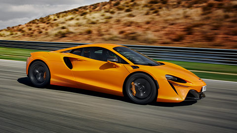 Side Shot Of Orange McLaren Artura Driving On Road