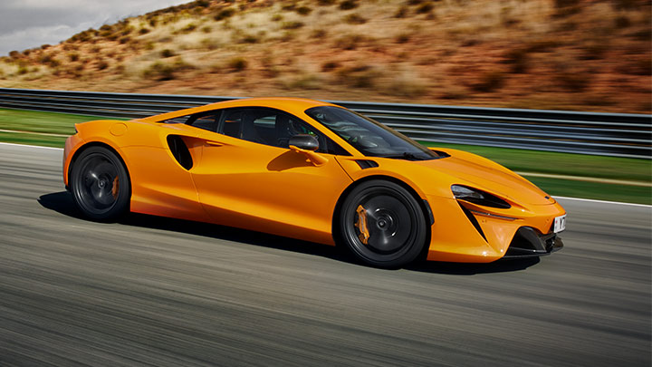 Side Shot Of Orange McLaren Artura Driving On Road