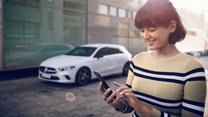 Mercedes-Benz owner booking service via smartphone, a-class parked in background