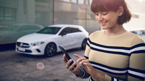 Mercedes-Benz owner booking service via smartphone, a-class parked in background