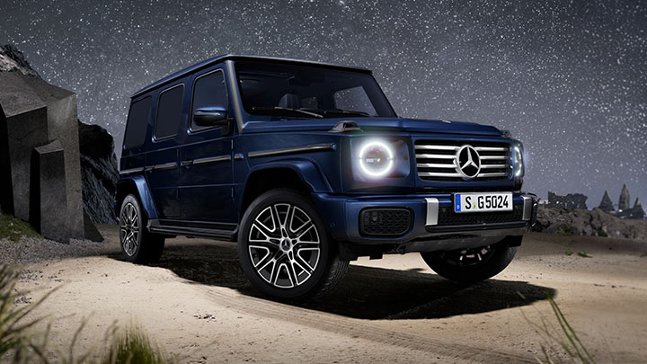 Navy blue Mercedes-Benz G-Class parked in front of a cave with a stary sky in the background
