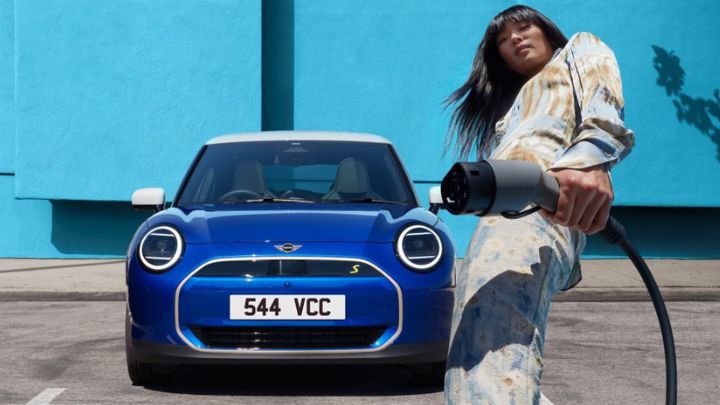 Woman holding an electric charger whilst standing in front of a blue MINI