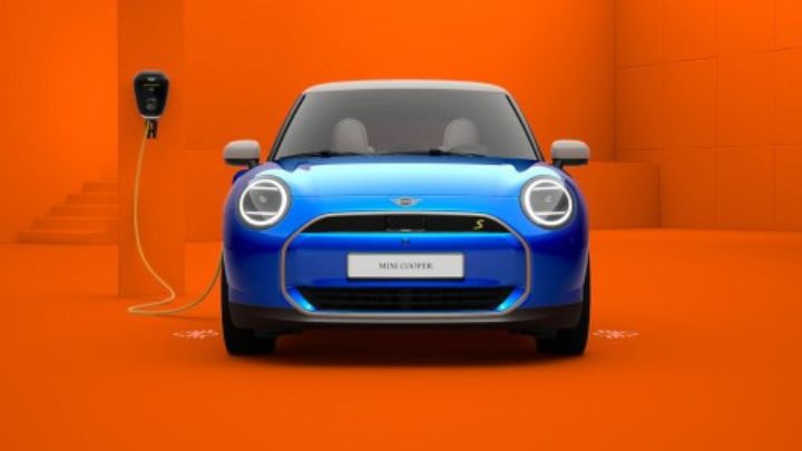 Blue MINI with a charging cable plugged into the vehicle and wall in front of a bright orange room