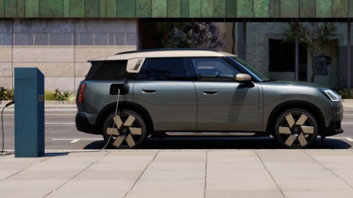 Silver MINI parked on the street with a charging cable plugged into the car and a street charging station.
