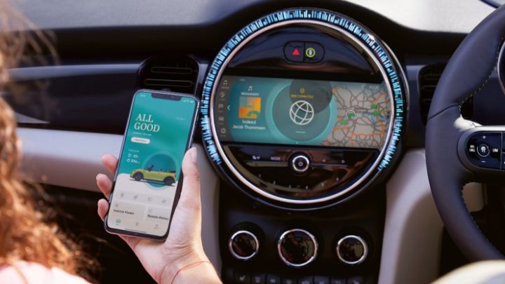 Woman holding a cell phone with MINI charging app open whilst sitting on the passenger seat in a MINI.