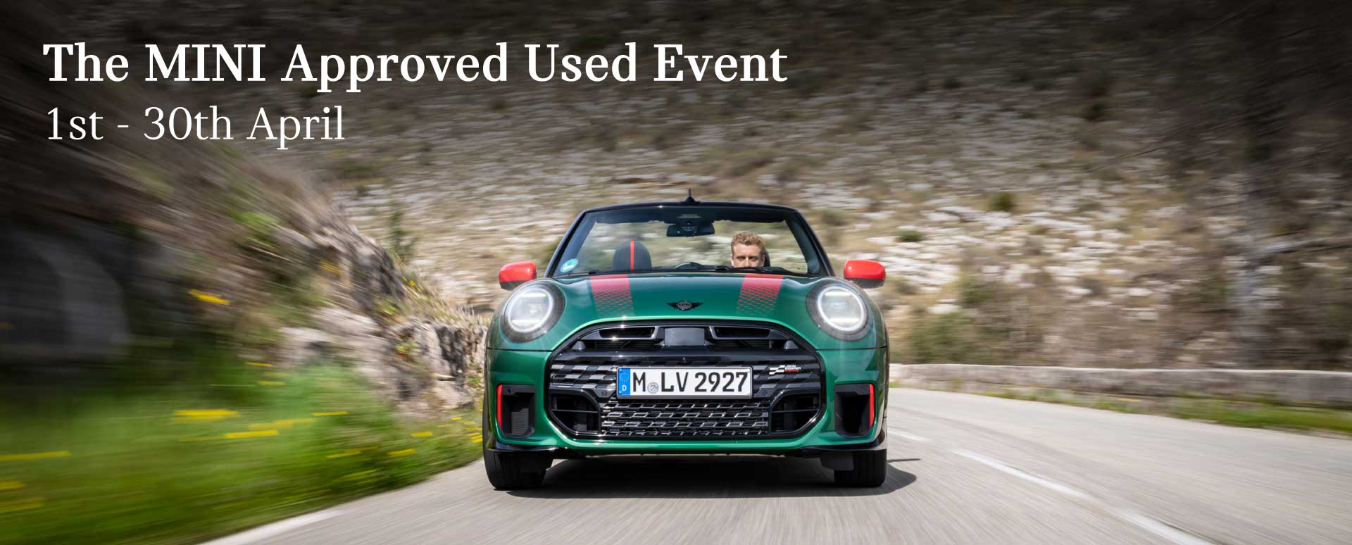 A front shot of a green MINI car with red accents driving with a rockey mountain backdrop. Promotional text overlay.