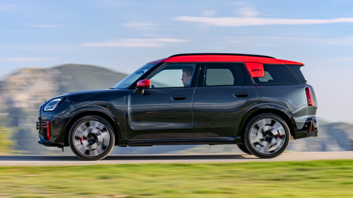 A fast driving black MINI vehicle with red trim.