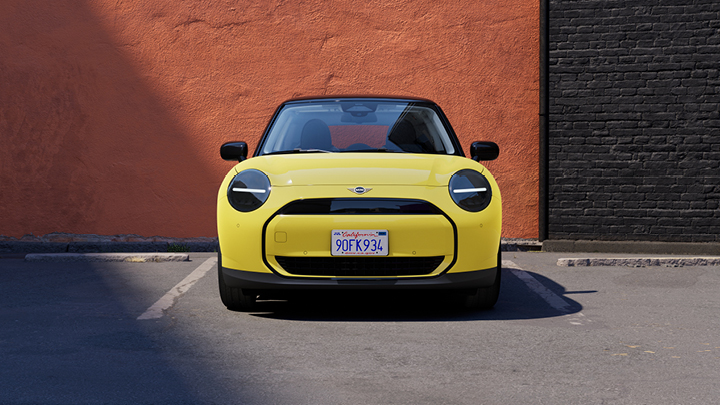 Front shot of Yellow MINI car parked in front of red brick wall.