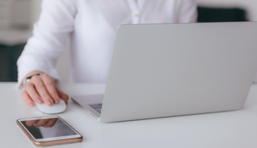 Person on their laptop with their phone on the table.