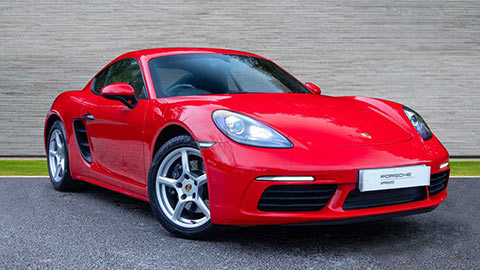Red Porsche 718 Cayman parked in front of a grey background