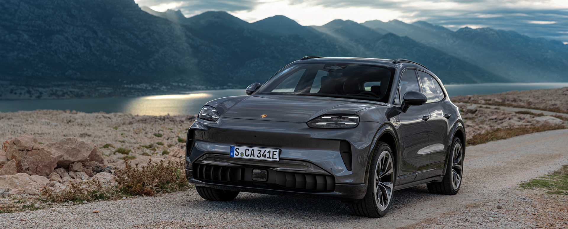 Grey Porsche Cayenne driving on dirt road at dusk.