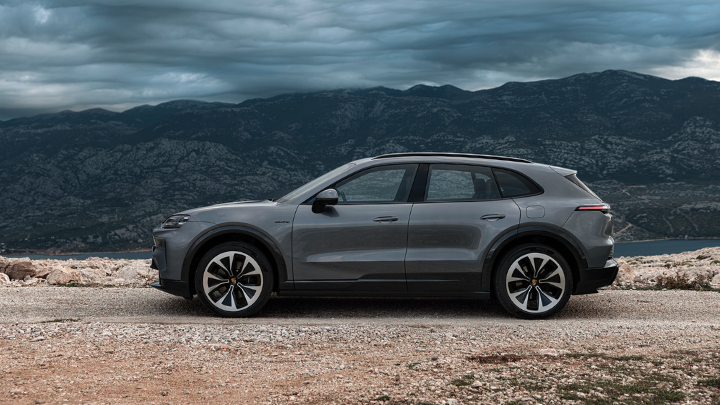 Grey Porsche Cayenne driving on dirt road at dusk.
