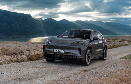 Grey Porsche Cayenne driving on dirt road at dusk.