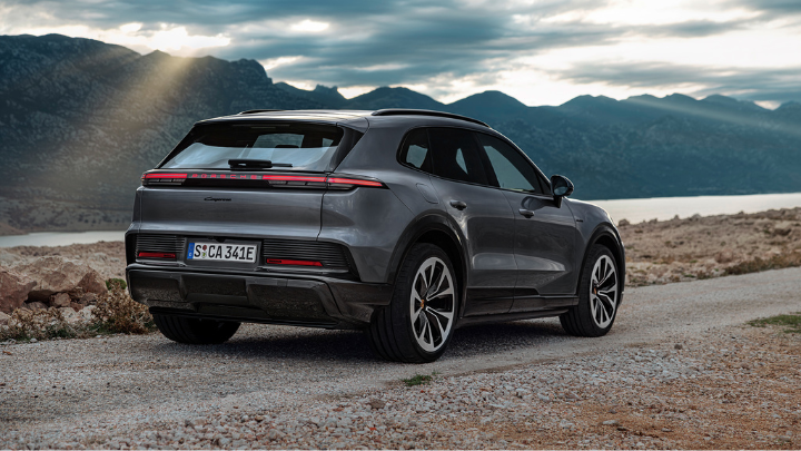 Grey Porsche Cayenne driving on dirt road at dusk.