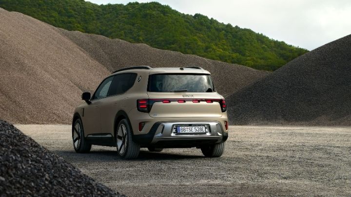 View of rear end of a smart #5 parked in front of piles of sand and rocks with trees in the background